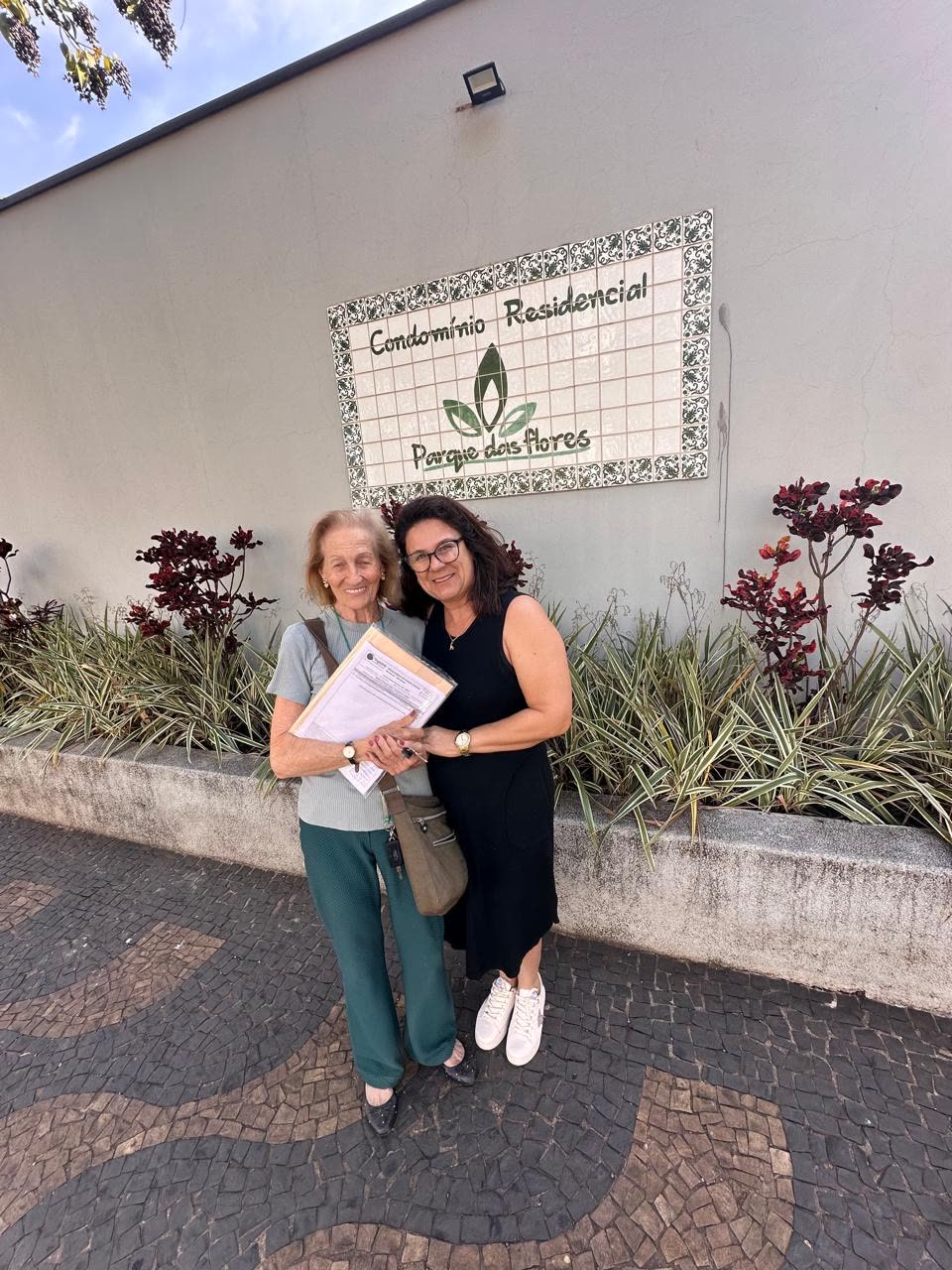 Cliente sorrindo ao receber a documentação do imóvel em frente ao Condomínio Parque das Flores